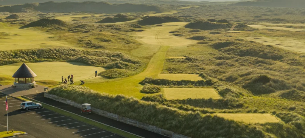 Aerial view of a scenic golf course with players, lush greens, and a clubhouse in the distance. Irish golfing experience.