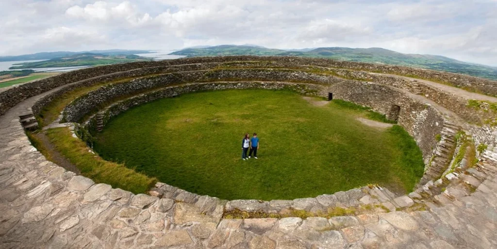 Visitors at the ancient stone fort in Ireland, showcasing lush green grass and stunning views. Historic site.