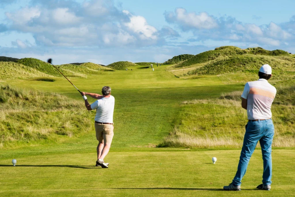 A golfer swings on a green course, surrounded by hills and blue skies, showcasing a vibrant golfing scene.