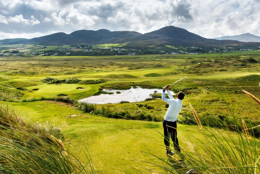 Golfer teeing off on a scenic Irish course, surrounded by lush greenery and mountains. Perfect day for golf!