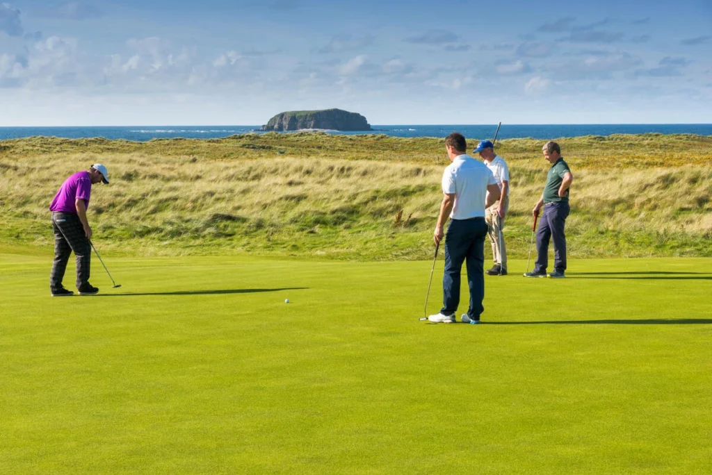 Four golfers putting on a lush green course, with a scenic coastal backdrop in Ireland. Perfect for golf enthusiasts.