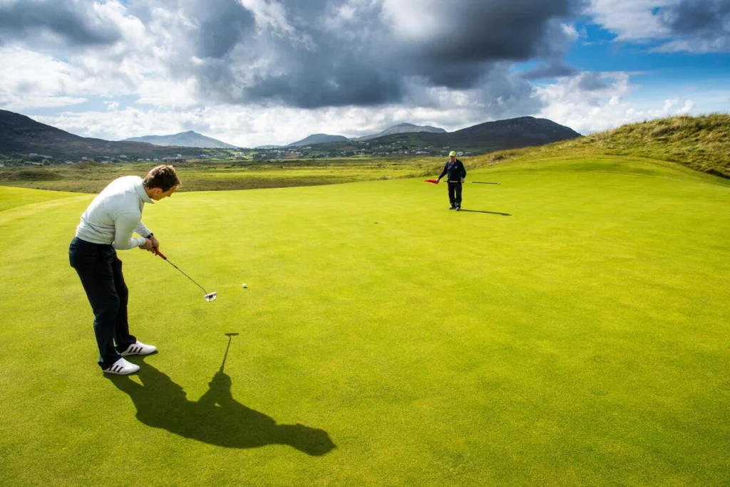 Golfer putting on a smooth green with mountains in the background. Beautiful Irish golf course scene.