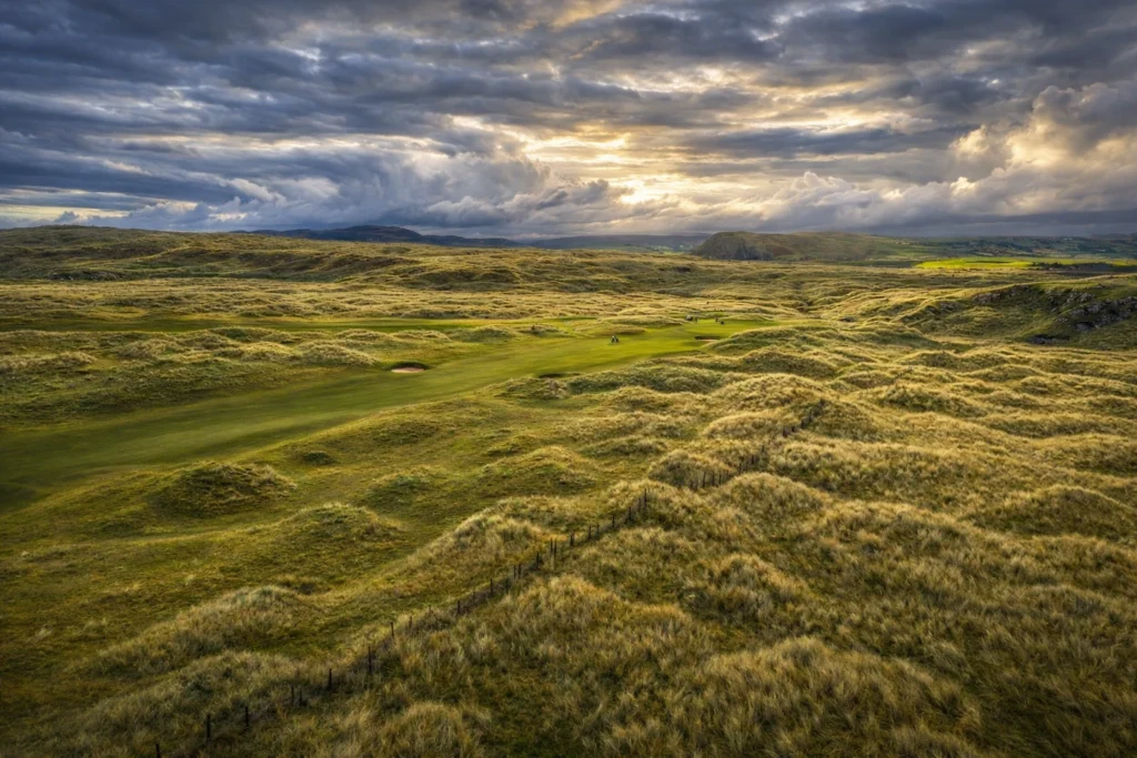 A stunning golf course at sunset, surrounded by lush green hills and dramatic skies in Ireland. Perfect for golf lovers.