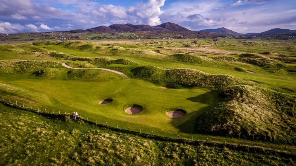Aerial view of a lush Irish golf course with rolling hills and sand traps under a dramatic sky. Perfect for golfers.