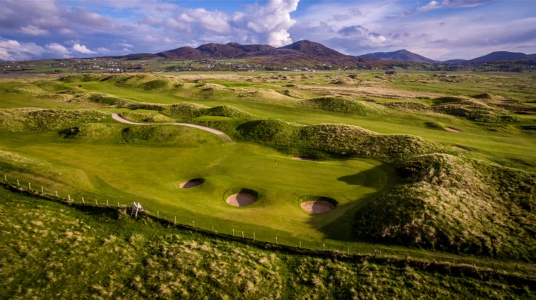 Aerial view of a lush Irish golf course with rolling hills and sand traps under a dramatic sky. Perfect for golfers.