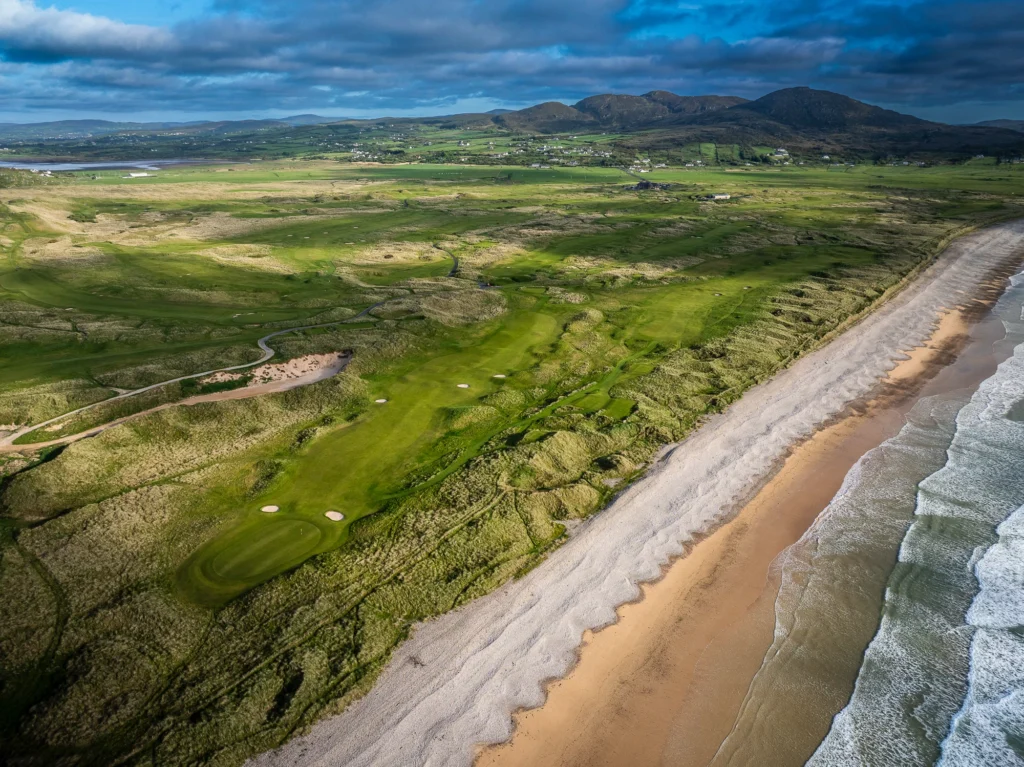 Aerial view of a lush golf course along a sandy beach in Ireland, highlighting scenic coastal landscapes.