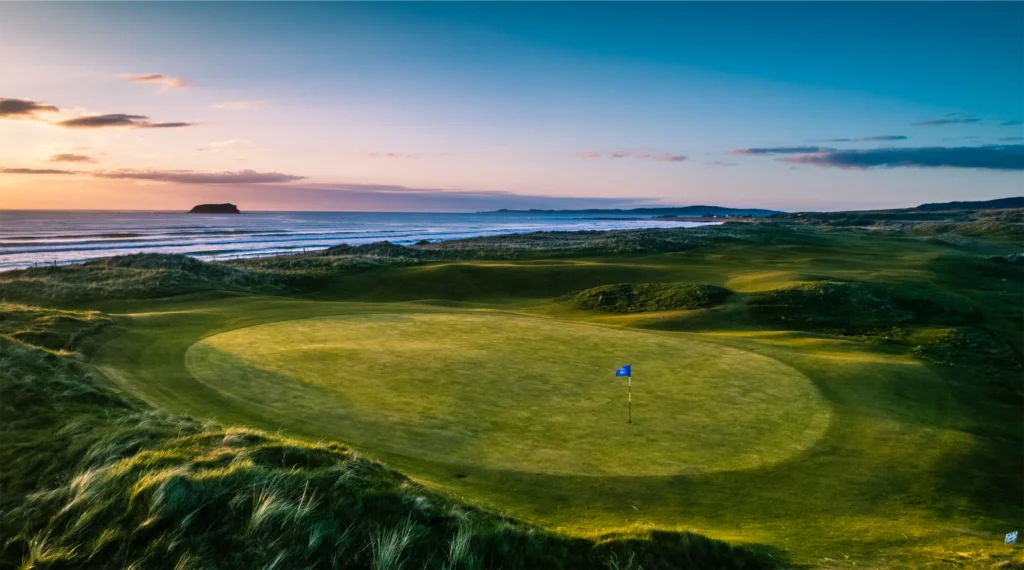 Stunning golf course at sunset, overlooking the ocean and distant hills. Perfect for seaside golfing adventures.