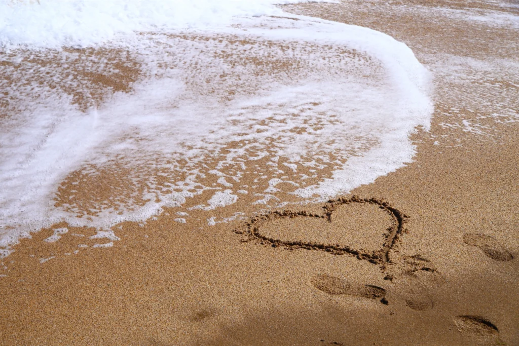 Heart drawn in sand along a beach, with gentle waves washing over. Perfect for beach lovers and romantic getaways.