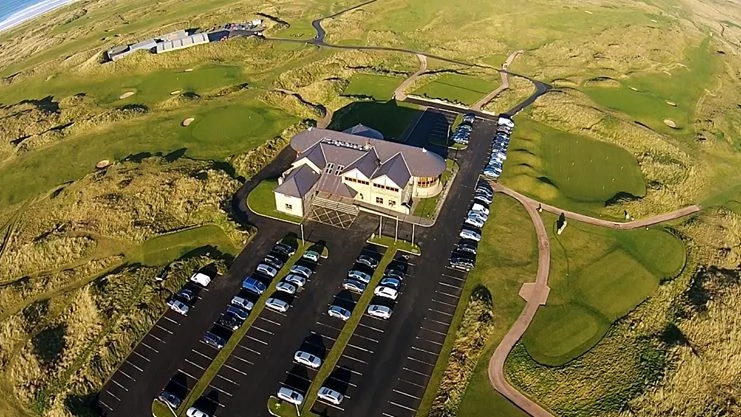Aerial view of a golf clubhouse with parking and lush green fairways in the background. Ideal for golf enthusiasts.