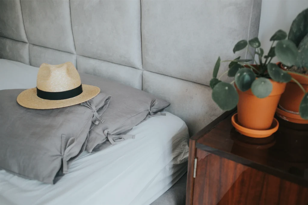 A stylish bedroom scene with soft pillows, a straw hat, and potted plants for a cozy vibe. Perfect for home decor.
