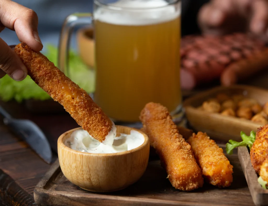 Crispy cheese sticks being dipped in creamy sauce, paired with a refreshing beer. Perfect pub snack!