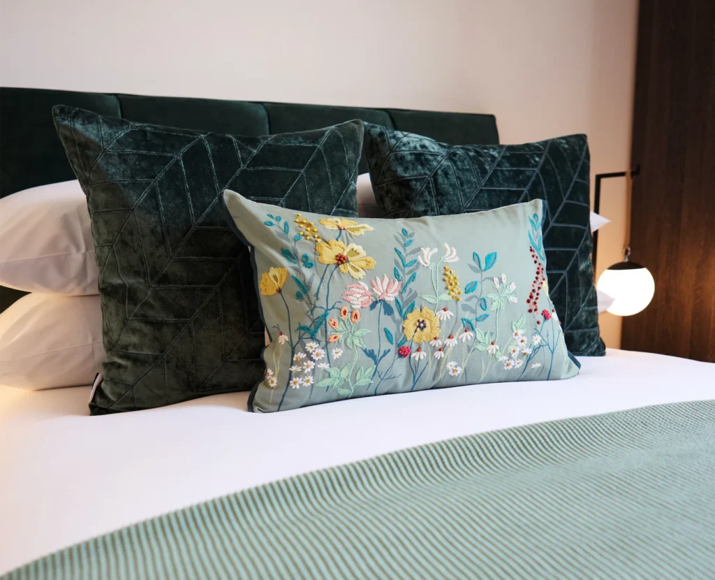 Stylish bed linens with floral embroidered pillows and plush green cushions, perfect for cozy decor.