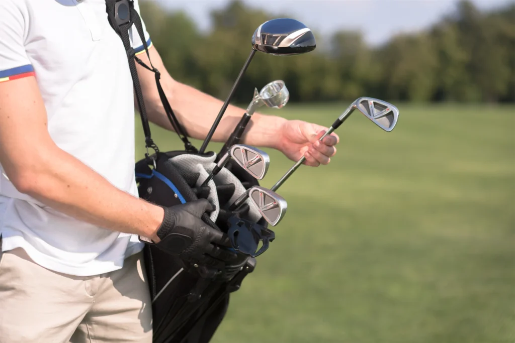 Golfer holding a golf bag with clubs on a sunny day. Perfect for golf enthusiasts and sports gear collections.