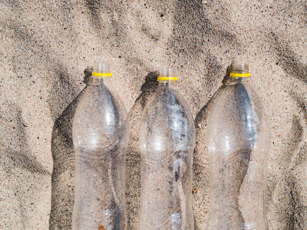 Three empty plastic bottles on sandy beach, highlighting littering issues and environmental concerns.