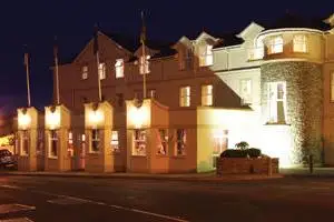 Brightly lit hotel exterior at night, offering accommodation and dining options in a charming Irish setting.