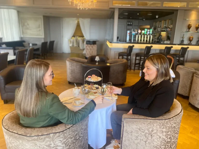 Two women enjoying afternoon tea in a stylish lounge, celebrating with drinks and pastries. Perfect for gatherings!