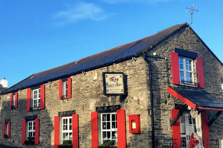 Nancy's Barn pub in Ballyliffin, featuring stone walls and bright red shutters, under a clear sky. Charming Irish pub.