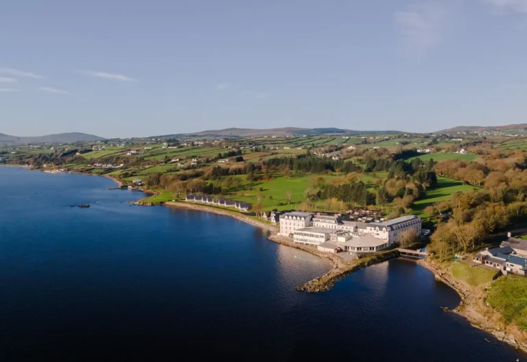 Scenic view of a waterfront hotel in Ireland, surrounded by lush green hills and tranquil waters. Perfect for retreats.