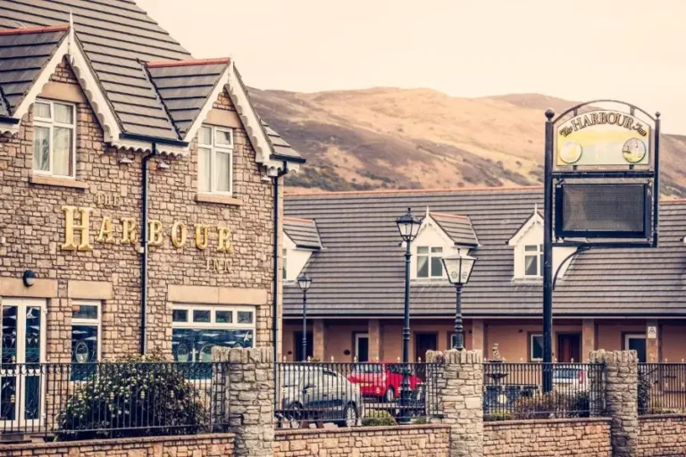 The Harbour Inn with stone façade, nearby accommodations, and scenic mountains. Ideal for a relaxing getaway.